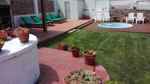A patio with a pool, green lawn, and lounge chairs.
