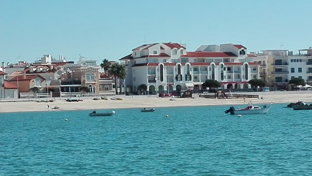 A coastal hotel with multiple balconies, a sandy beach, and boats in the water.