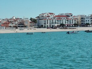 A coastal hotel with multiple balconies, a sandy beach, and boats in the water.
