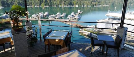 Una terraza con mesas y sillas con vistas a un puerto deportivo y barcos.