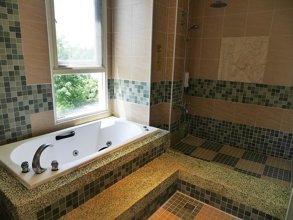 A bathroom with a bathtub, shower, and a window providing a view of greenery.