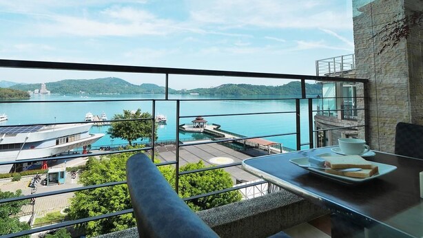 A balcony with a view of a lake, a dock, and a building with solar panels. - Cherng Yuan Hotel (Yuchi)