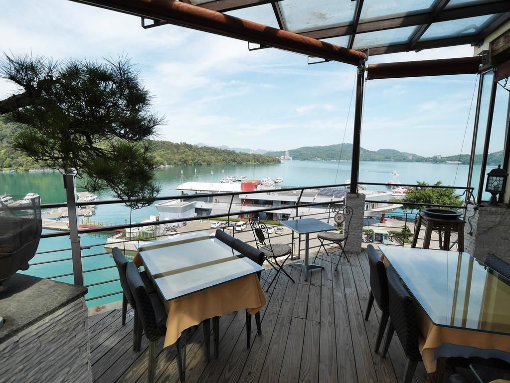 Una terraza de madera con mesas y sillas que da a un puerto deportivo con barcos y un lago.