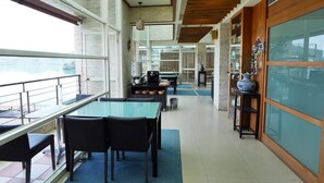 A spacious indoor area with a glass wall overlooking a body of water, featuring a dining area with tables and chairs, a kitchen area, and a decorative vase on a shelf. - Cherng Yuan Hotel (Yuchi)