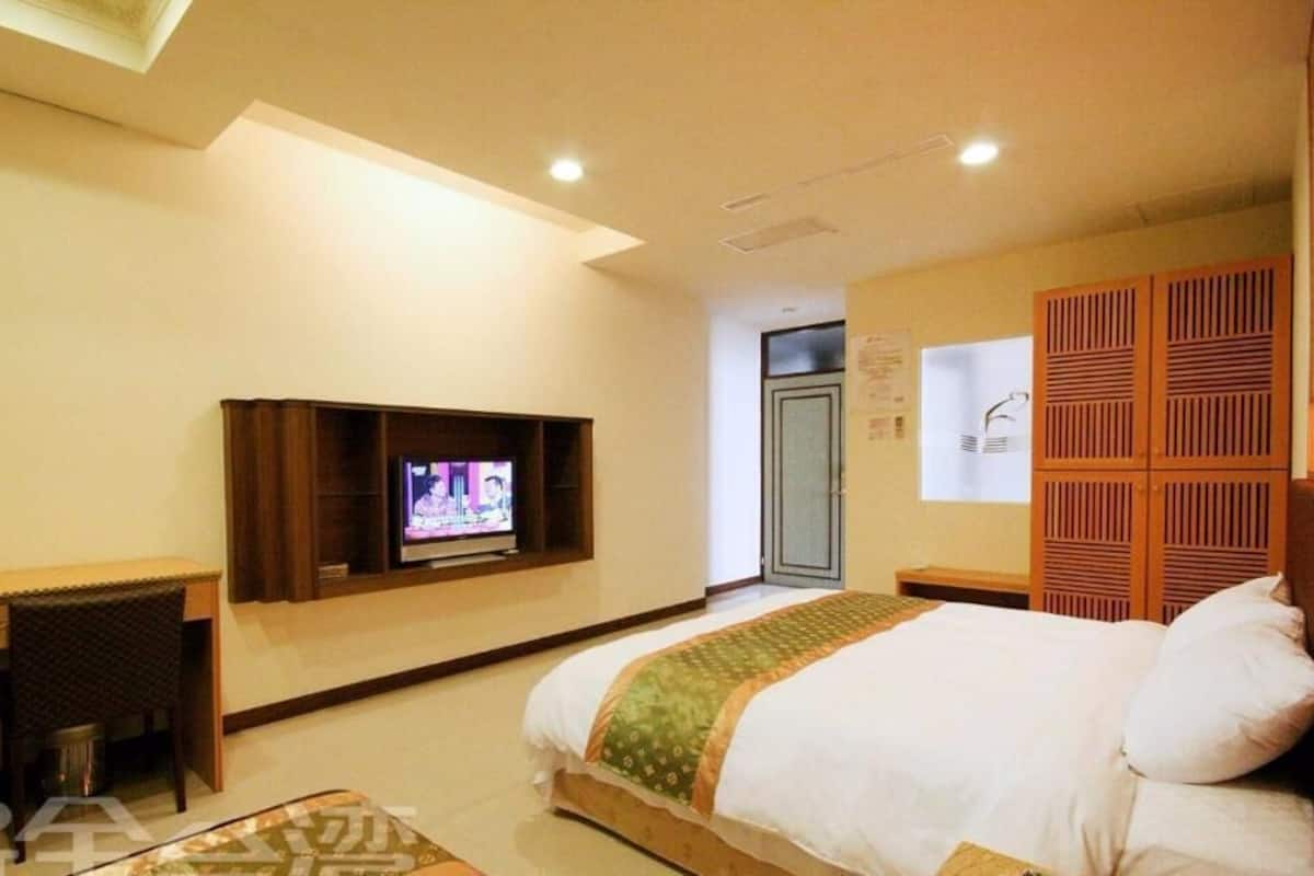 Una habitación de hotel con una cama, televisión montada en la pared, una mesita y un armario.