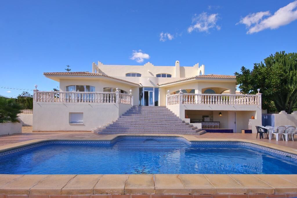 Une grande maison avec une piscine, un escalier menant à l’entrée et du mobilier d’extérieur.