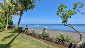 A beach with palm trees, a stone wall, and a small boat in the water. - Modern, Luxury and Spacious Beach front Villa with Private Pool & Staff (Dencarik / Lovina)