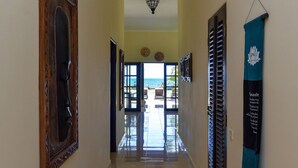 A hallway with a wooden door, a hanging light fixture, and a view of the ocean through glass doors. - Modern, Luxury and Spacious Beach front Villa with Private Pool & Staff (Dencarik / Lovina)