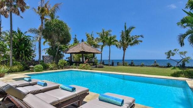 A poolside area with lounge chairs and a thatched-roof gazebo overlooking the ocean. - Modern, Luxury and Spacious Beach front Villa with Private Pool & Staff (Dencarik / Lovina)