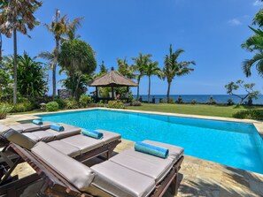 A poolside area with lounge chairs and a thatched-roof gazebo overlooking the ocean. - Modern, Luxury and Spacious Beach front Villa with Private Pool & Staff (Dencarik / Lovina)