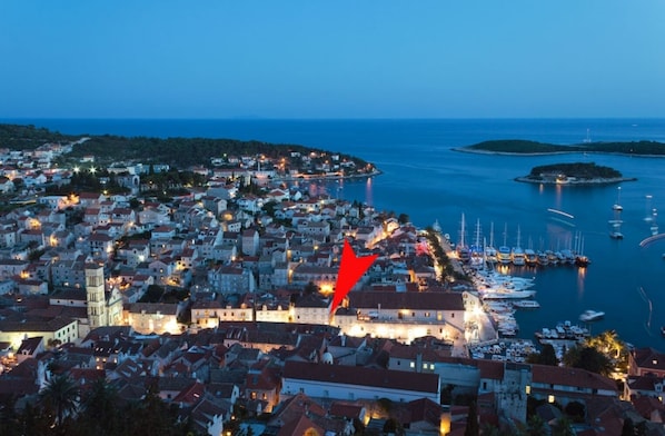 Un pueblo costero al atardecer con edificios históricos, un puerto deportivo y una flecha roja destacada que apunta a un lugar específico.