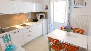 Eine kleine Küche mit weißen Schränken, einer Mikrowelle, einem Toaster und einem Spülbecken. Ein Esstisch mit orangefarbenen Stühlen und eine Vase mit Blumen sind ebenfalls vorhanden.