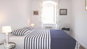 Ein Schlafzimmer mit einem Bett, zwei Nachttischlampen, einem Fenster mit Vorhängen und zwei gerahmten Bildern an der Wand.