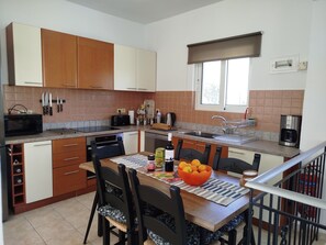A modern kitchen with wooden cabinets, a dining table with chairs, a microwave, a toaster, and a coffee maker. - Relaxing stunning villa, wonderful views , large pool, 
 short walk to village. (Chania)