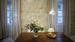 Un comedor con pared de piedra, una mesa de madera, un jarrón con flores y una cesta de frutas.