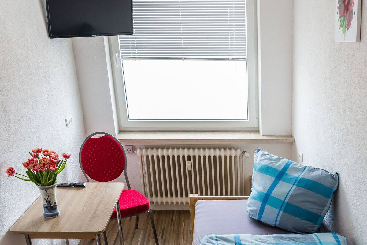 A small, tidy room with a bed, a desk, a chair, and a TV mounted on the wall.