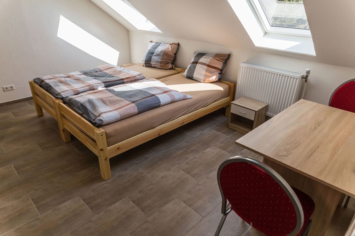 A bedroom with a wooden bed, a small table, a red chair, and a skylight.