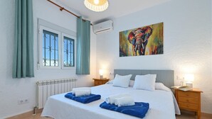 Une chambre d’hôtel avec un grand lit, deux tables de chevet, une fenêtre avec des rideaux, un appareil de climatisation et un tableau représentant un éléphant.