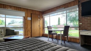 Een kamer met een bed, een tafel met stoelen, een televisie en grote ramen met uitzicht op het omliggende landschap.