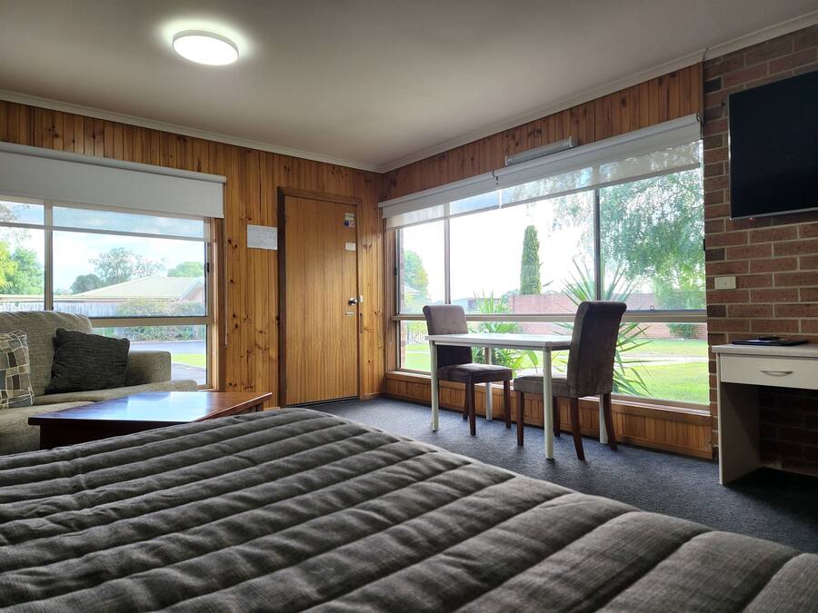 Habitación con cama, una mesa y sillas, televisión y ventanas amplias con vistas al exterior.