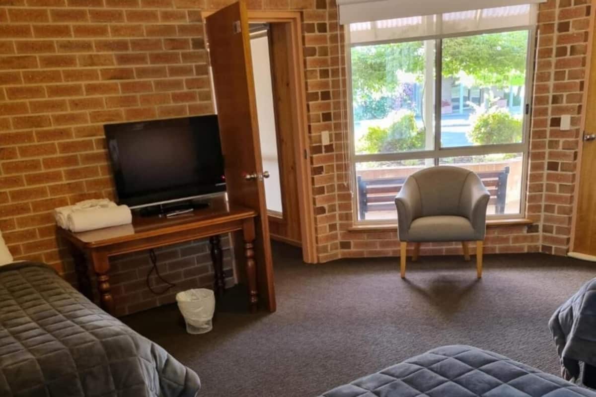 Ein Hotelzimmer mit zwei Betten, einem Fernseher, einem Sessel und einem großen Fenster.