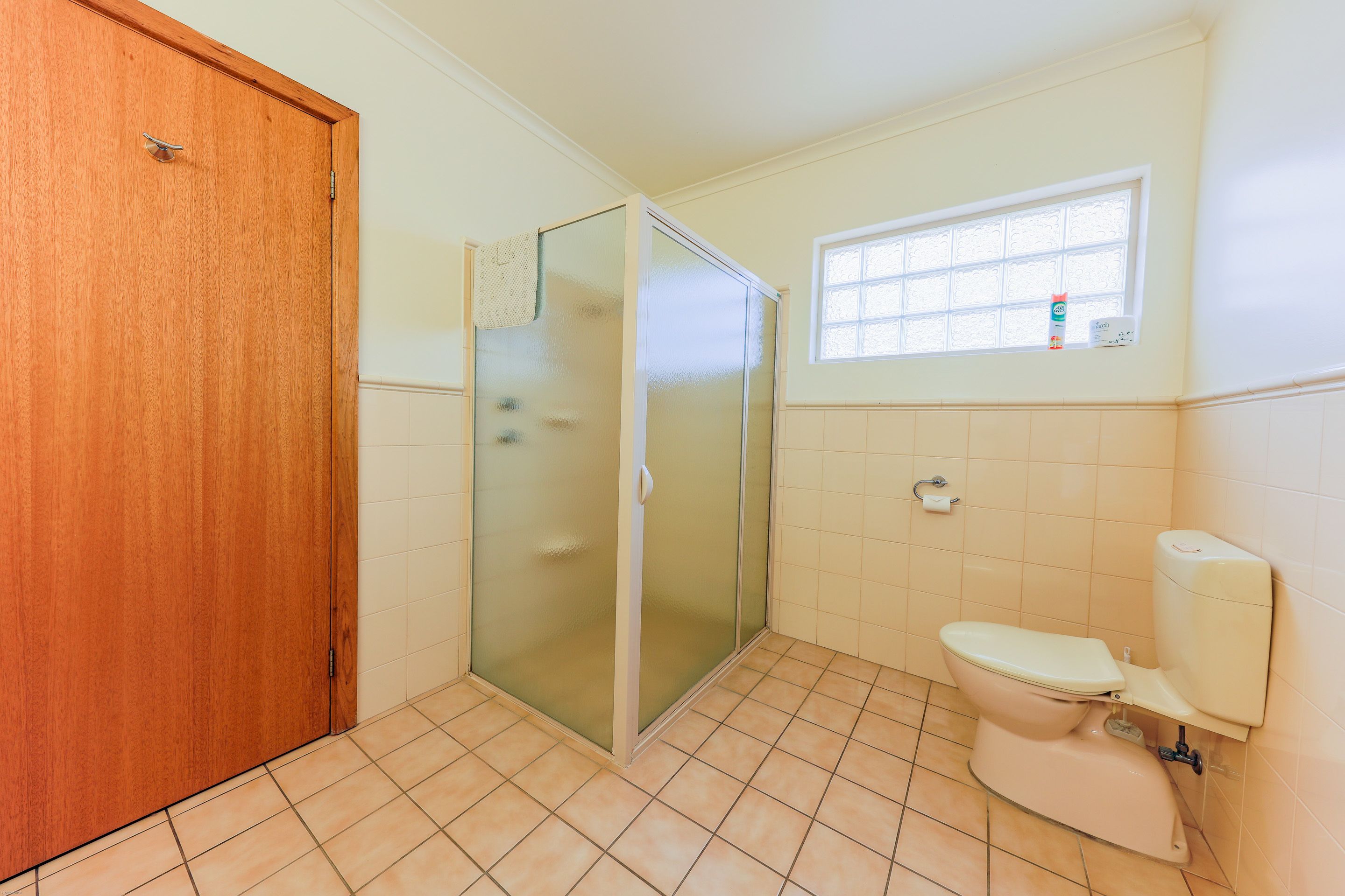 Une salle de bain avec une porte en bois, une douche en verre, des toilettes et une fenêtre donnant sur l’extérieur.