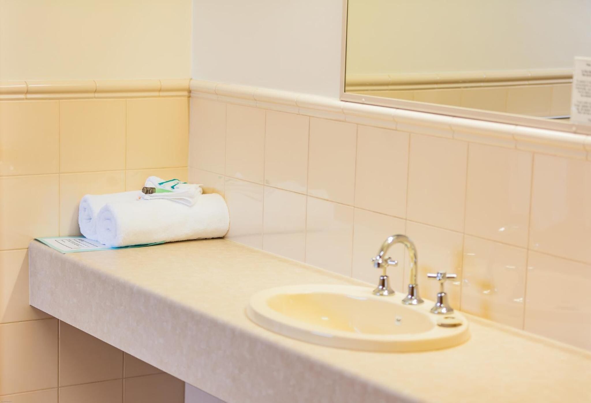 Un baño con lavamanos, espejo y toalla sobre la encimera.