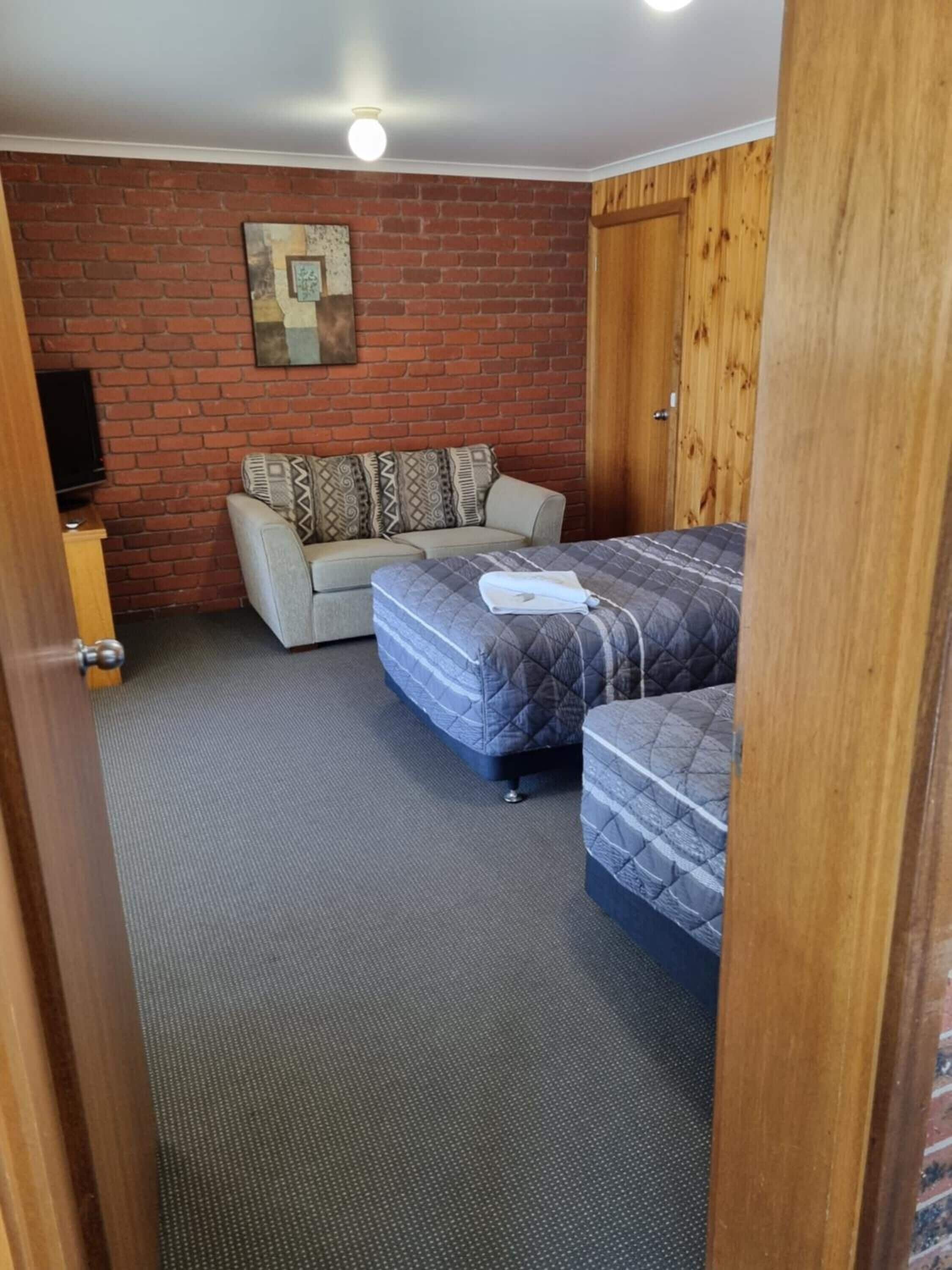 Ein Zimmer mit Backsteinwand, Holztür, einer Couch und zwei Betten.