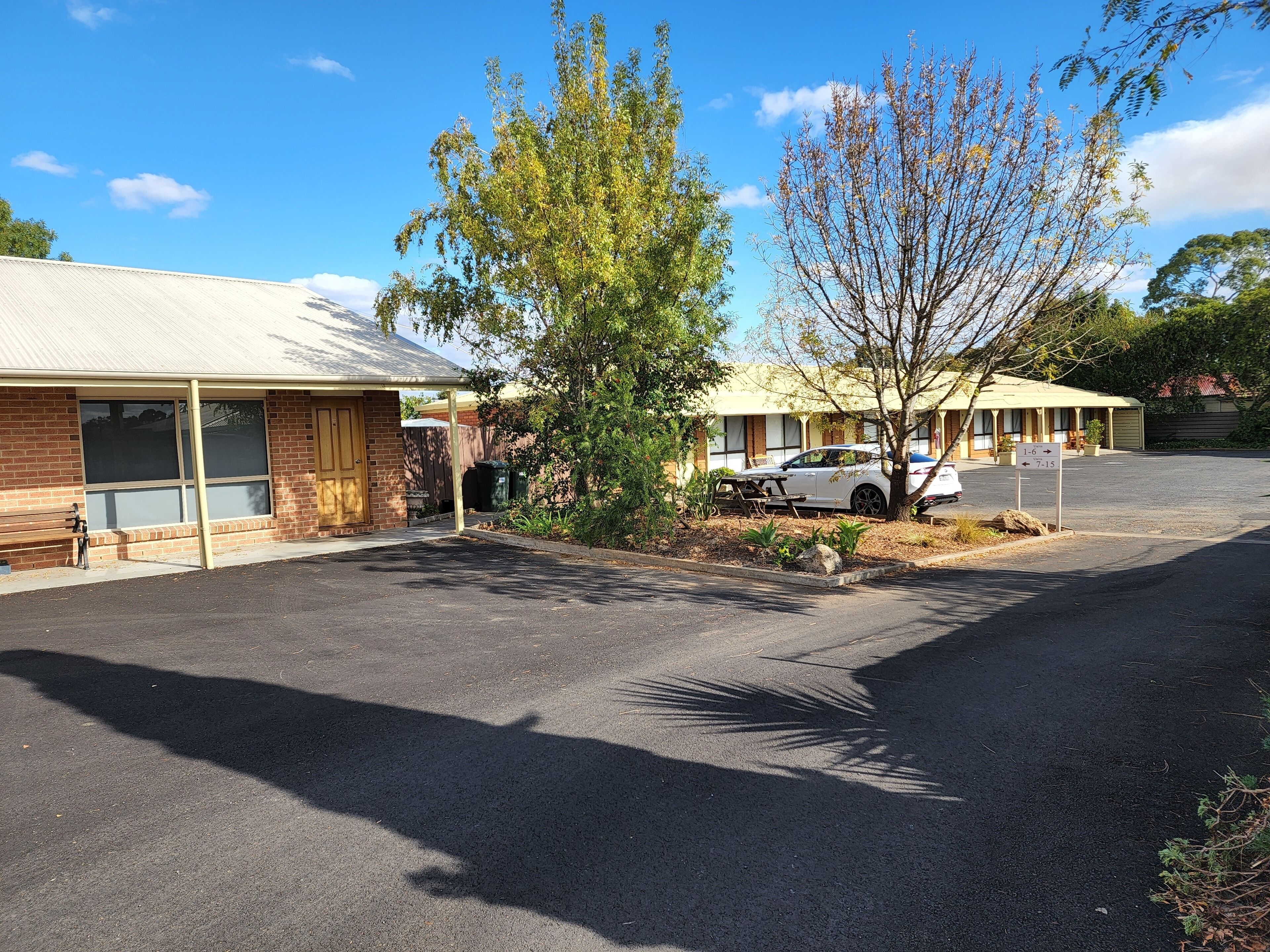A motel with a covered parking area, a picnic table, and a sign indicating room numbers.