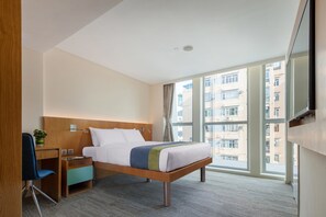 Ein Hotelzimmer mit einem Bett, einem Schreibtisch, einem Sessel, einem Fernseher und großen Fenstern.