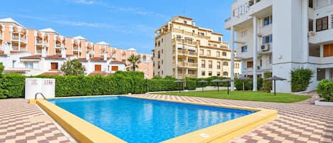 A swimming pool with a checkered floor, surrounded by multi-story buildings with balconies and a clear sky.