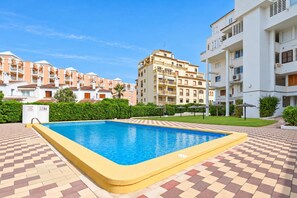 Une piscine dont le fond est recouvert de carreaux, entourée d’immeubles à plusieurs étages dotés de balcons, sous un ciel dégagé.