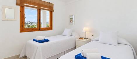 Habitación de hotel con dos camas, ventana con vistas, ventilador de techo y mesita de noche con lámpara.