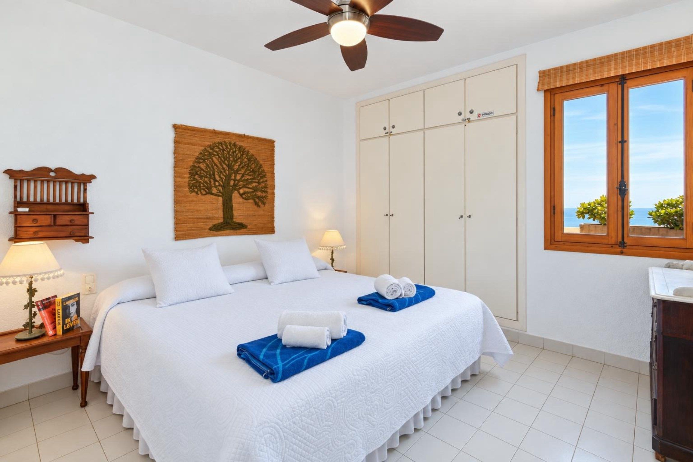 A hotel room with a bed, a wardrobe, a window with a view, and a ceiling fan.