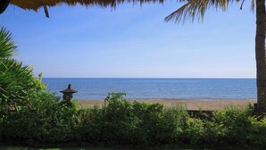 A beach view with a thatched roof structure, palm trees, and a stone lantern. - Villa Bundar: fabulous beachfront villa with pool and with staff! (Dencarik / Lovina)