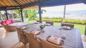 An outdoor dining area with a wooden table set for four, surrounded by wicker chairs, overlooking a beach. - Villa Bundar: fabulous beachfront villa with pool and with staff! (Dencarik / Lovina)
