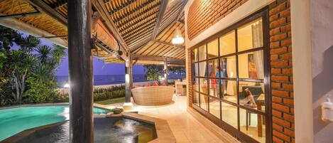 A pool area with a hot tub, surrounded by a covered patio with brick walls and large windows.