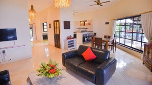 A spacious living room with a black leather sofa, a TV mounted on the wall, and a dining area with a table and chairs. - Villa Bundar: fabulous beachfront villa with pool and with staff! (Dencarik / Lovina)
