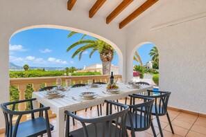A dining area with a table set for four, surrounded by chairs, with a view of a pool and palm trees.