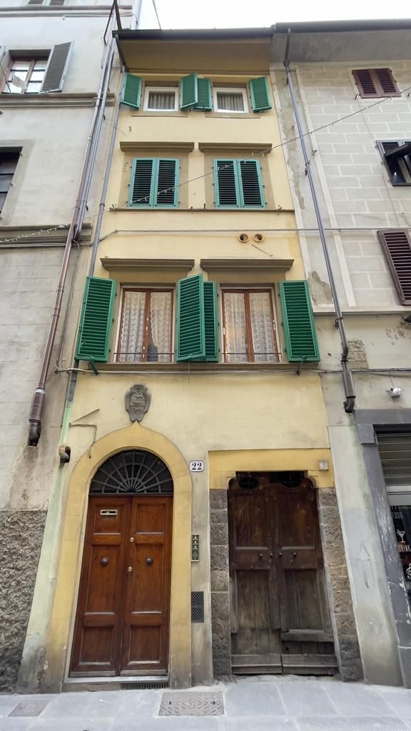 A multi-story building with a central entrance featuring two wooden doors, green shutters on windows, and a stone facade.
