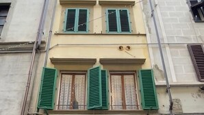 Un edificio de varios pisos con una entrada central que presenta dos puertas de madera, contraventanas verdes en las ventanas y fachada de piedra.