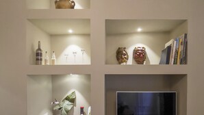 Una pared con varios estantes mostrando libros, un televisor y objetos decorativos.