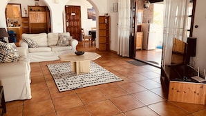 Sala de estar con sofá blanco, una mesita de centro y alfombra estampada. Se ve un área de cocina a través de un arco.