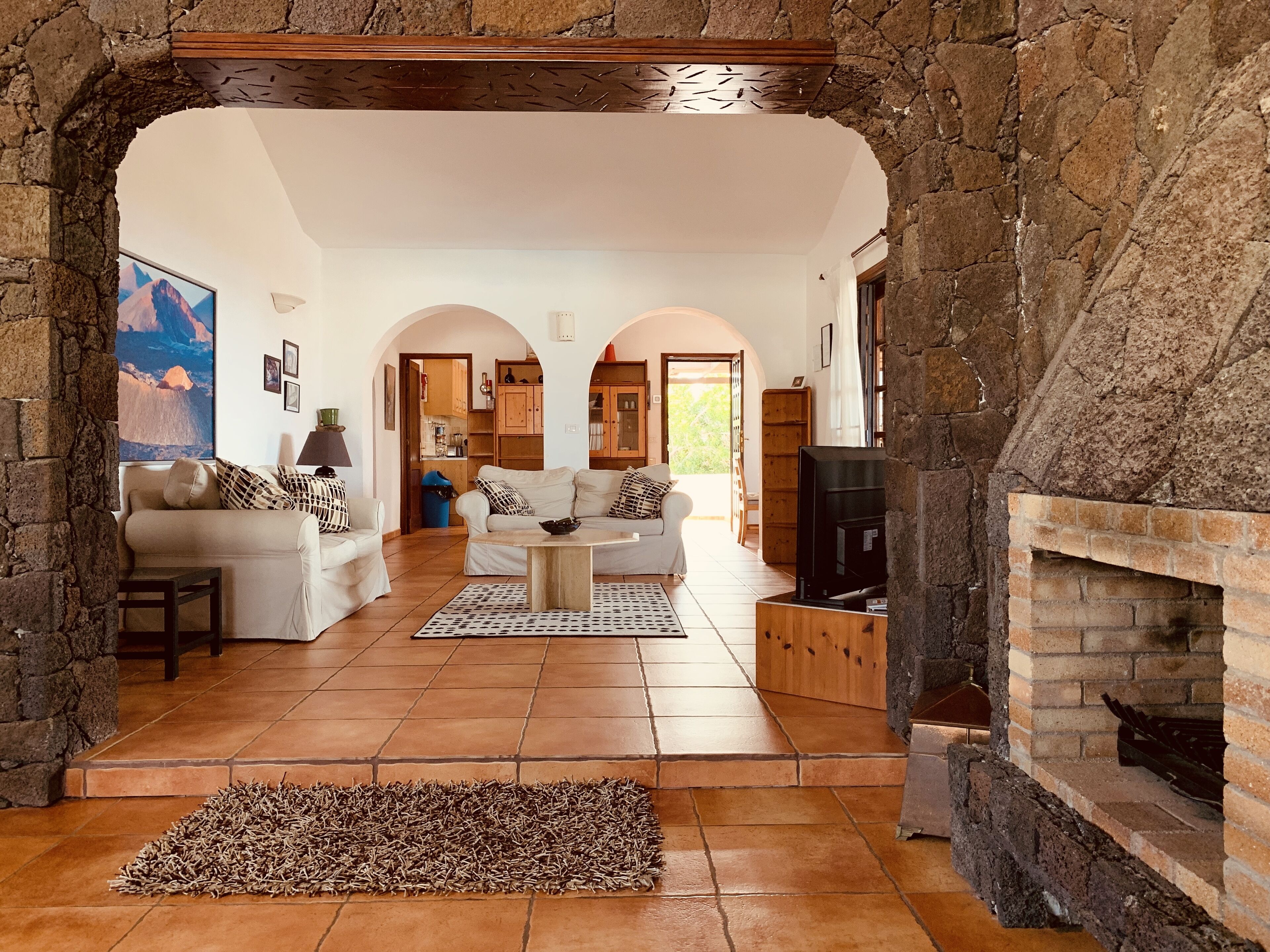 A spacious living room with a stone archway, a fireplace, and a television.