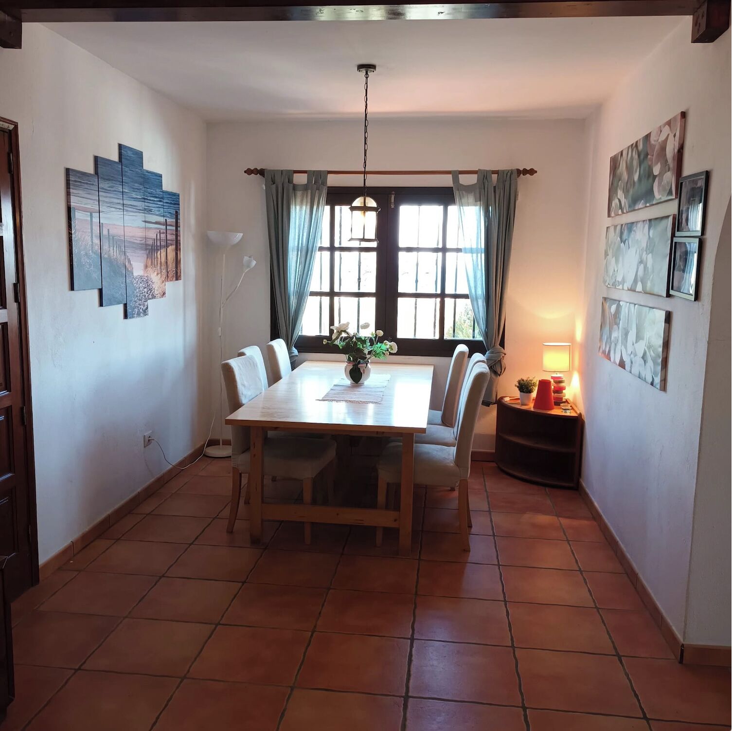 A dining area with a wooden table, chairs, a vase of flowers, and artwork on the walls.
