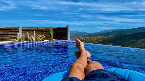 A person relaxing by an infinity pool with a view of mountains and cacti. - Four Storey Finca  Infinity Pool Mountain Views optional separate apartment  (Malaga Province)