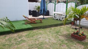 A backyard with a lawn, a wooden chair, a table, and a planter with flowers. - Gîte Muskad, Creole charm and tropical calm at Cap Chevalier (Sainte Anne)