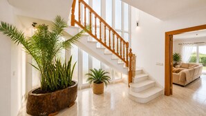 A spacious living area with a wooden staircase, large windows, and potted plants.