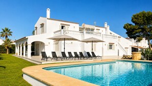 A white villa with a swimming pool, sun loungers, and a covered patio area.