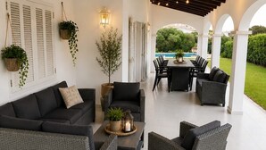 A covered outdoor patio with wicker furniture, a dining table, and hanging plants.